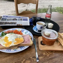 Ontbijtbord met spiegelei, ham en toast op een terras, met koffie en Coca-Cola
