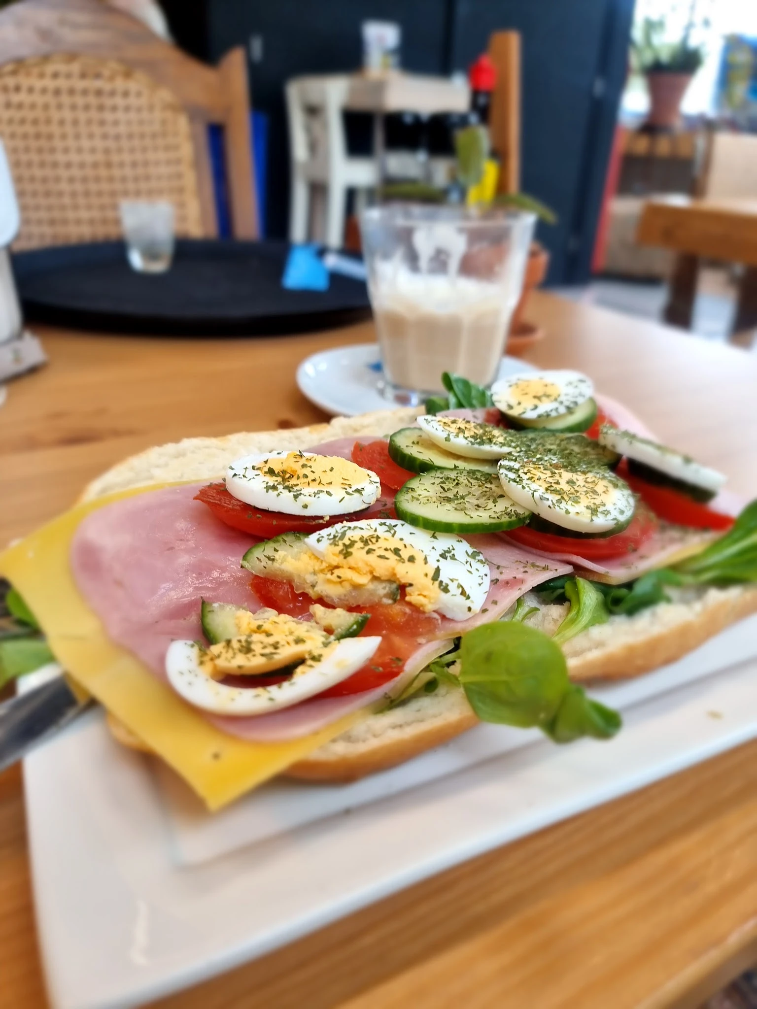 Broodje met ham, gekookte eieren, tomaat en komkommer met kruiden op een bord, met glas melk op achtergrond