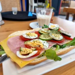 Broodje met ham, gekookte eieren, tomaat en komkommer met kruiden op een bord, met glas melk op achtergrond