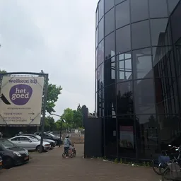 Extern zicht op moderne glazen gevel van kringloopwinkel met welkombord aan zijkant, parkeerplaats en fietsen vooraan