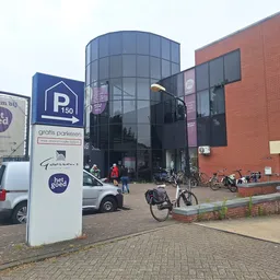 Voorkant van kringloopwarenhuis met rode bakstenen gevel, glazen ingang en parkeerterrein met fietsen