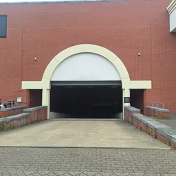 Rode bakstenen gevel met grote halfronde ingang en zwarte deur van kringloopwarenhuis