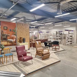 Winkelvloer met uitgestalde meubels en fauteuils, stellingen met artikelen op achtergrond, moderne industriële winkelruimte