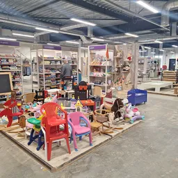 Winkelvloer met speelgoed en kindermeubels uitgestald, achtergrond toont stellingen met diverse goederen