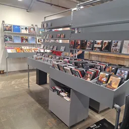 Grijze winkelkasten met dvd's, cd's en andere media uitgestald, samt wandstellingen met merchandise