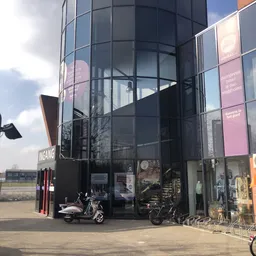 Moderne glazen gevel van kringloopwinkel met zwarte ramen en roze borden, scooter en fietsen voor de ingang