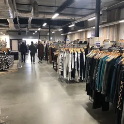 Winkelvloer van kringloopwinkel met kledingrekken vol tweedehands kleding, bezoekers lopen rond tussen de stellingen