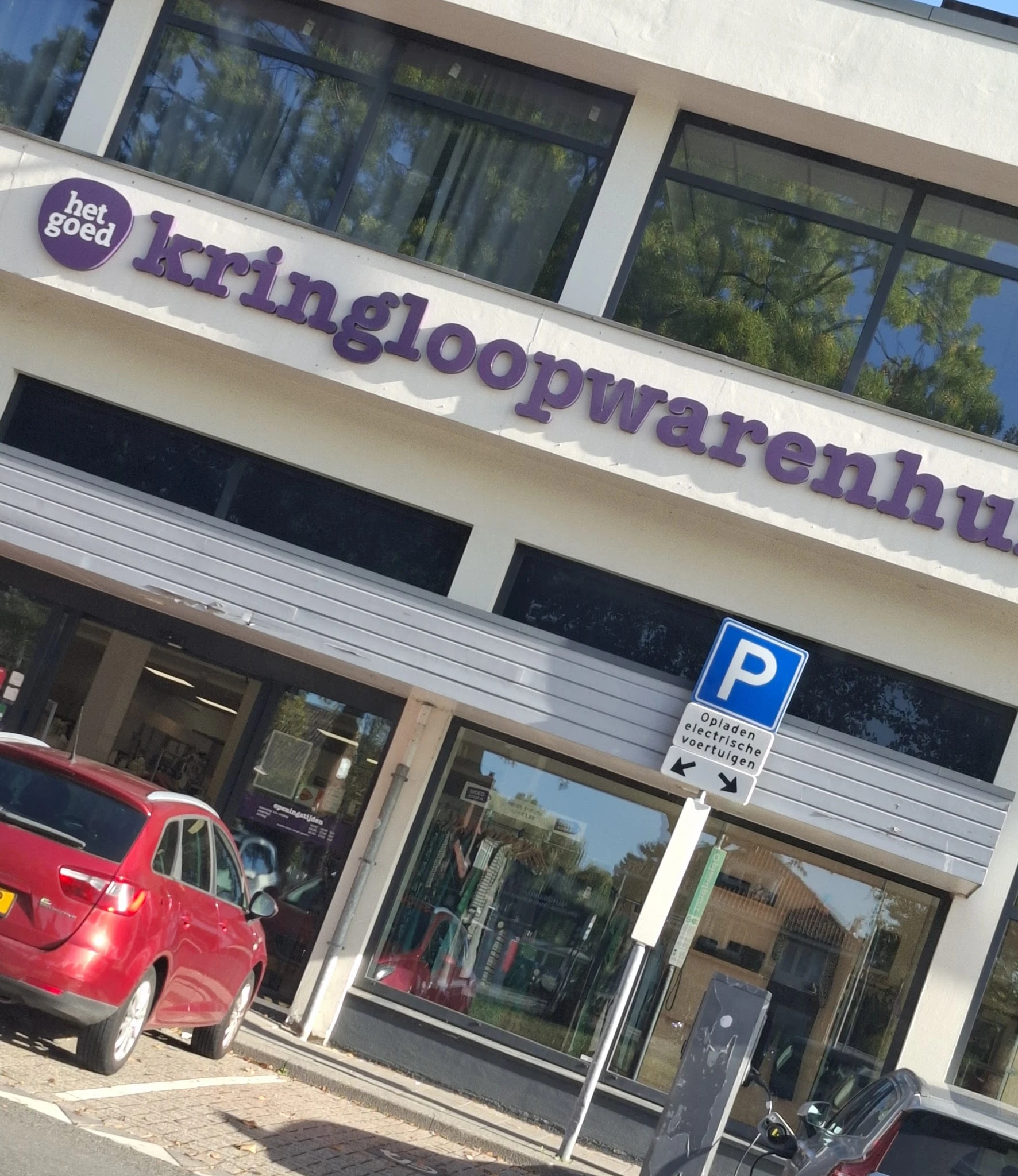 Winkelpui met paars logo en naam 'kringloopwarenhuis' boven de ingang, parkeerplaats aanwezig