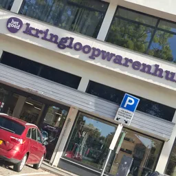 Winkelpui met paars logo en naam 'kringloopwarenhuis' boven de ingang, parkeerplaats aanwezig