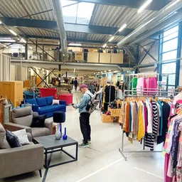 Ruim winkelbinnenaanzicht met kleding op rekken, meubels en bezoekers in kringloopwarenhuis
