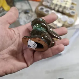 Close-up van een bruine en groene glazen vogelfiguur in een hand
