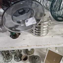Close-up van een grijs deksel met label nummer 109 en stapel zilveren metalen schalen op witte plank