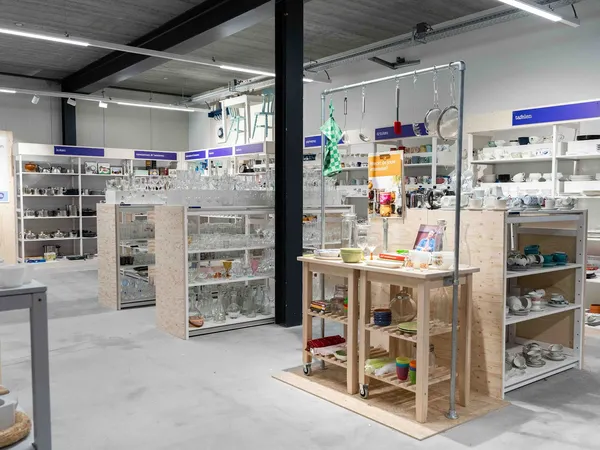 Overzicht van de winkelvloer met verschillende stellingen, vitrines en een houten display-tafel vol met huishoudelijke spulle