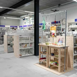 Overzicht van de winkelvloer met verschillende stellingen, vitrines en een houten display-tafel vol met huishoudelijke spulle