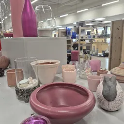 Uitgestalde huishoudelijke items: roze en witte serviesgoed, kaarsen, glazen en decoratieve objecten op een witte tafel in de