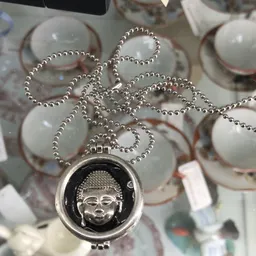 Zilveren kettinghanger met Boeddha-motief op zilveren balletjesketting, naast witte decoratieve ballen