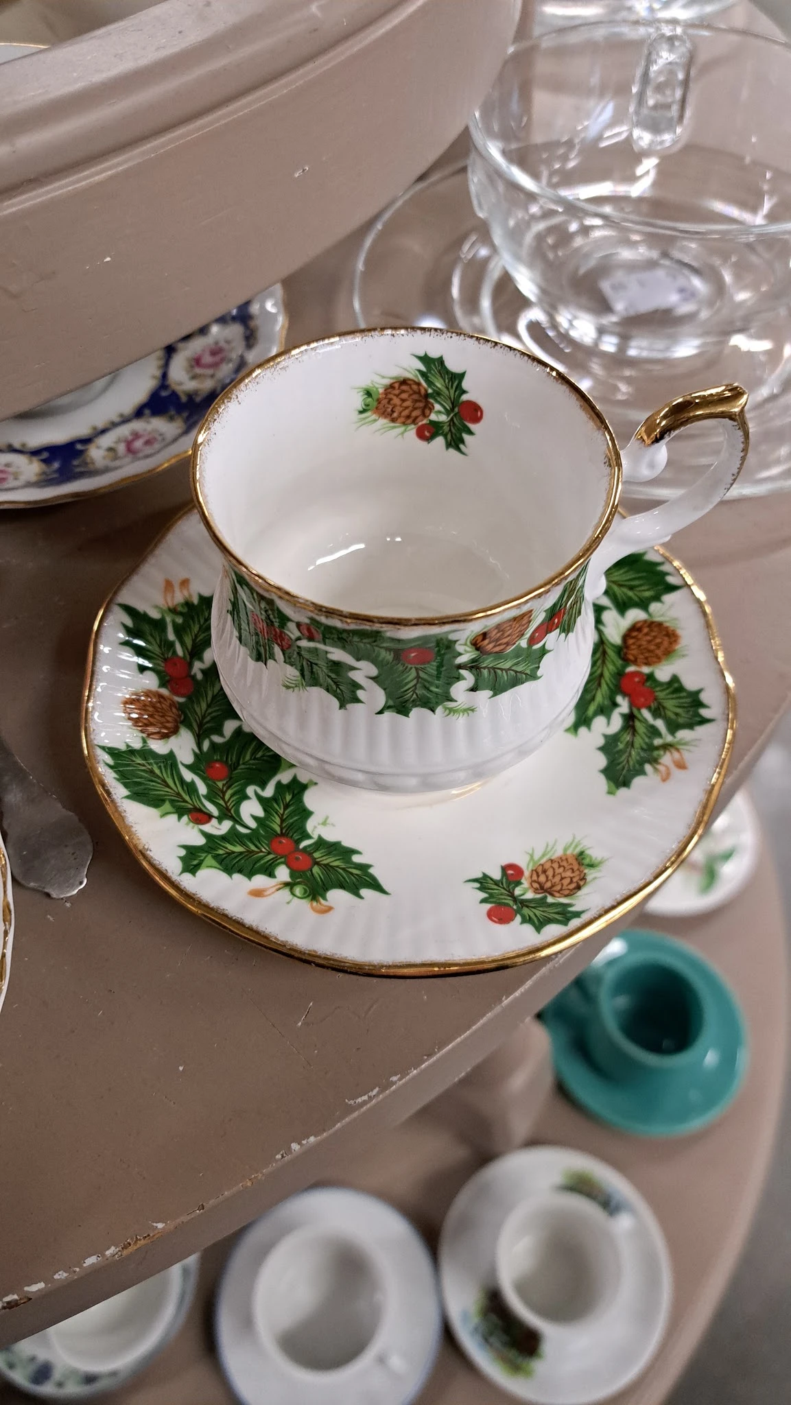 Porseleinservies met kerstmotief: kopje en schotel met gouden rand en afbeelding van hulst en dennenappels