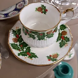 Porseleinservies met kerstmotief: kopje en schotel met gouden rand en afbeelding van hulst en dennenappels