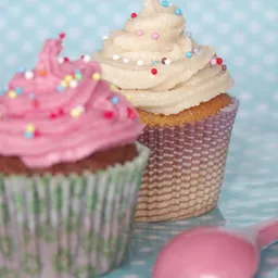 Twee versierde cupcakes met roze en beige frosting en gekleurde bolletjes op lichtblauwe achtergrond