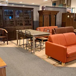Winkelvloer met diverse meubels: oranje bank, eettafel met stoelen, houten kasten en fauteuils