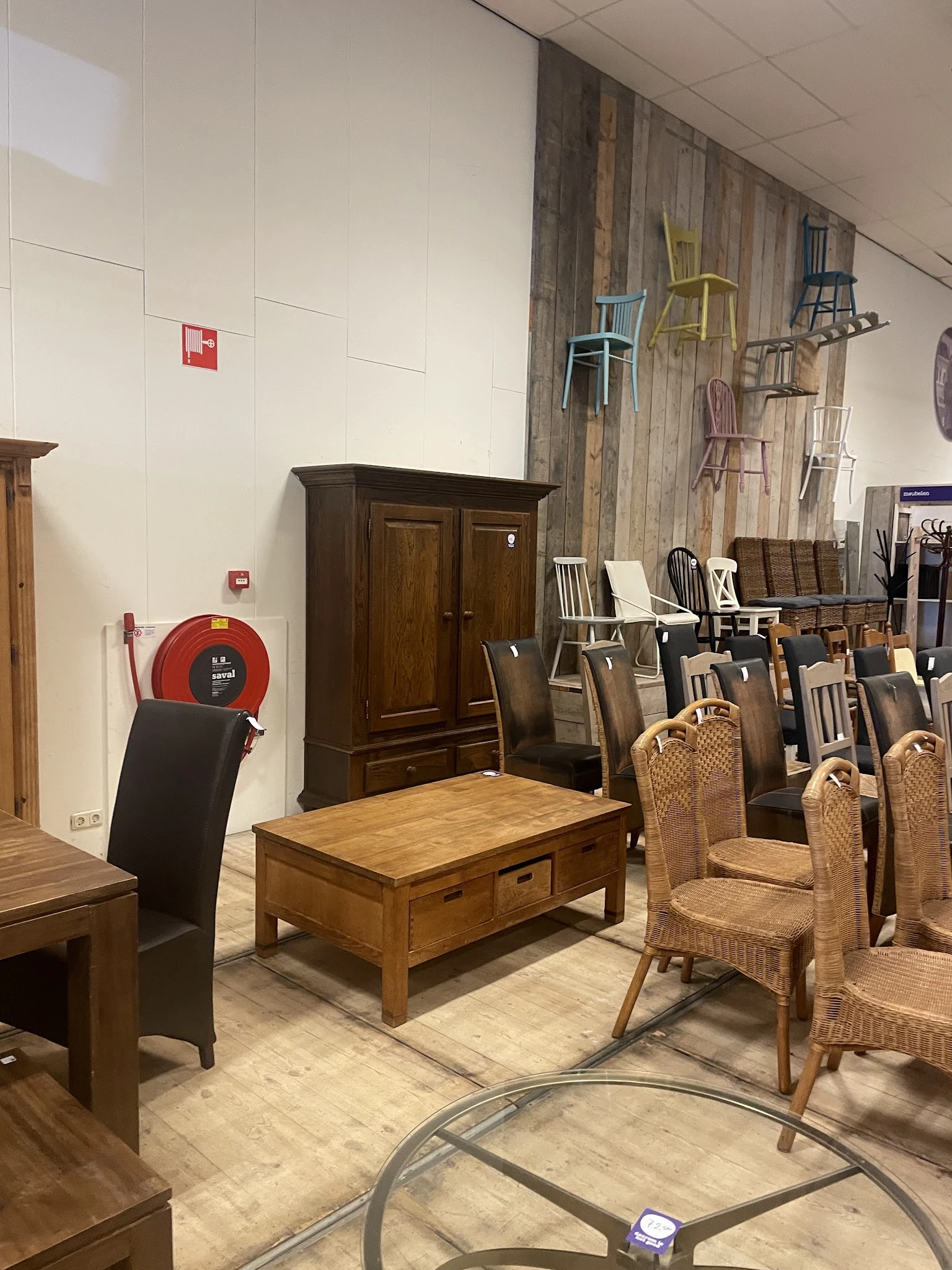 Winkelvloer met houten meubels: tafels, stoelen en een kast, naast een rode brandblusser