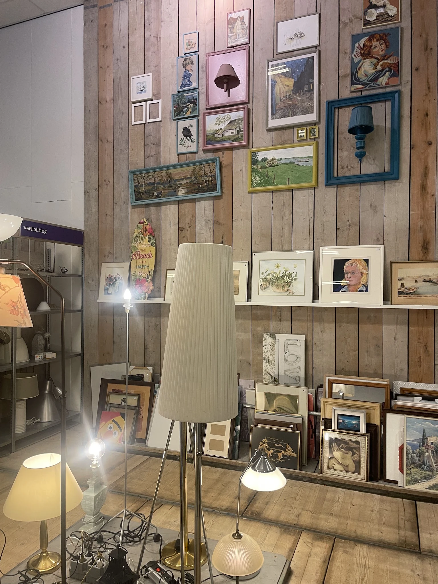 Wanddisplay met uitgestalde kunst, prenten, fotolijsten en decoratieve items in een kringloopwinkel