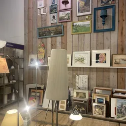 Wanddisplay met uitgestalde kunst, prenten, fotolijsten en decoratieve items in een kringloopwinkel