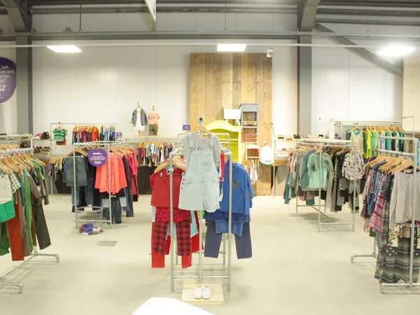 Ruime winkelvloer met kledingrekken vol tweedehands kleding voor kinderen, goed verlicht met industriële verlichting