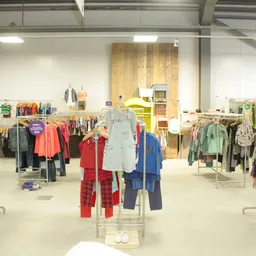 Ruime winkelvloer met kledingrekken vol tweedehands kleding voor kinderen, goed verlicht met industriële verlichting
