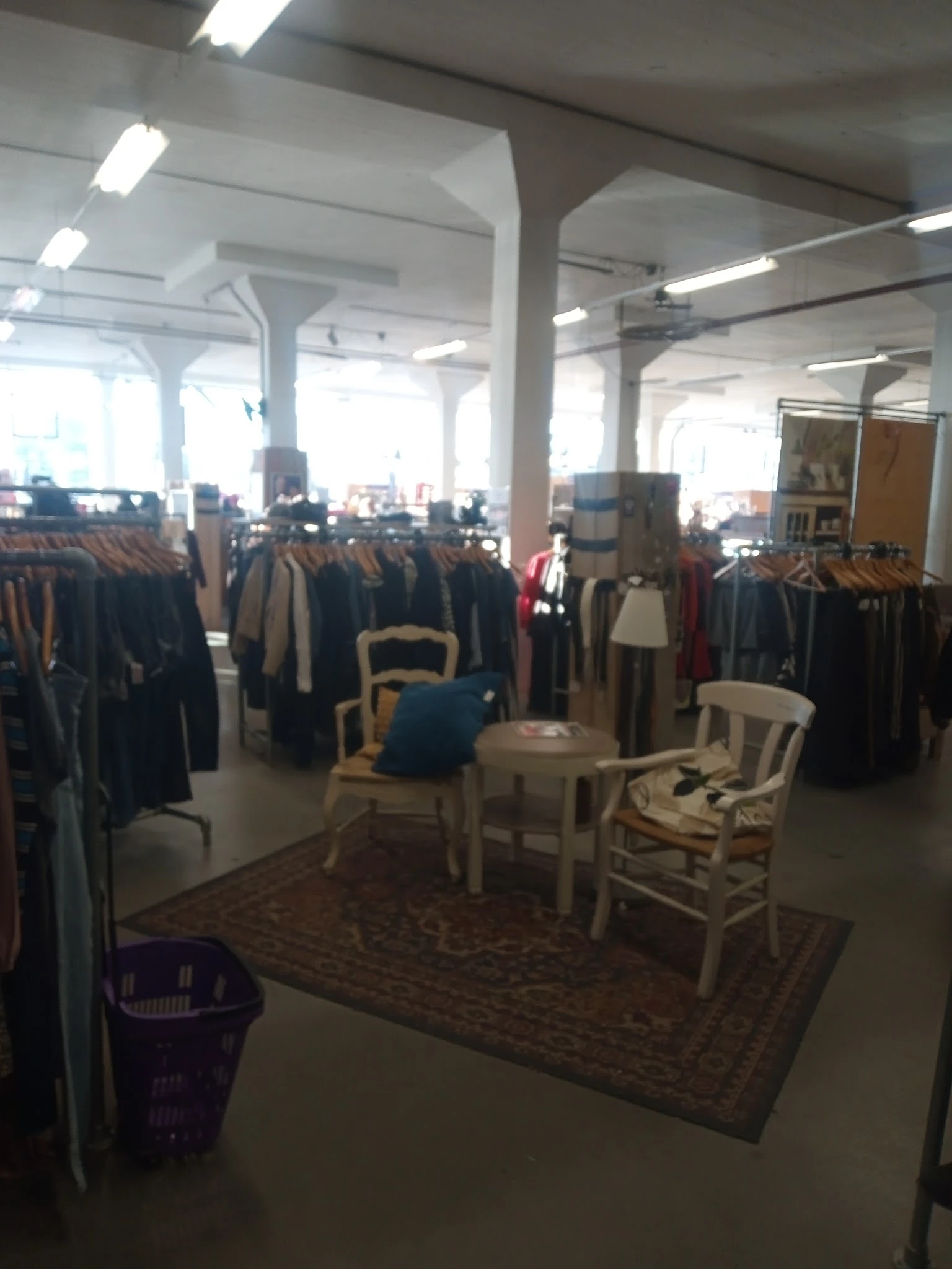 Winkelinterieur met kledingrekken vol tweedehands kleding, zithoek met stoelen en tafeltje in het midden