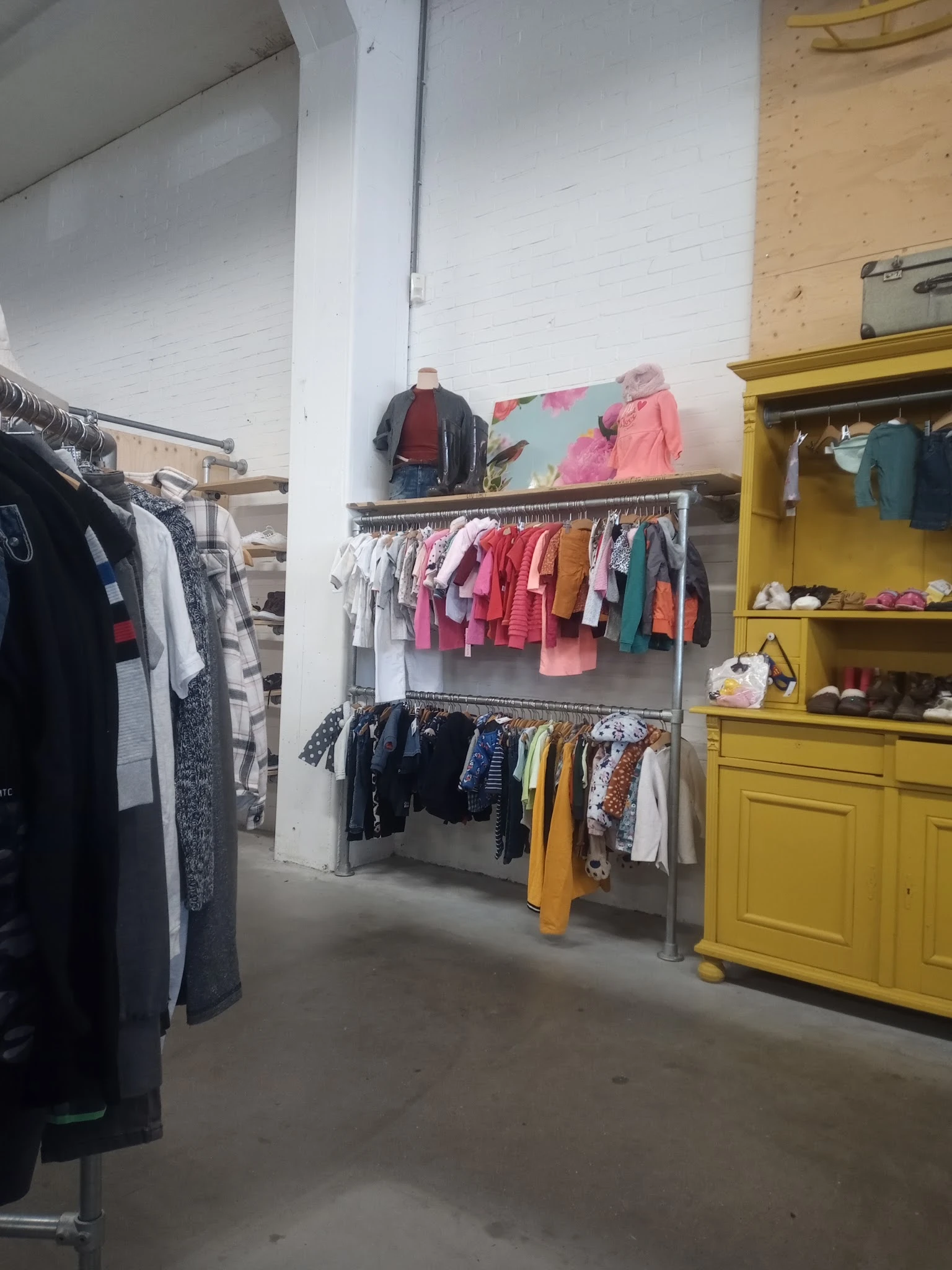 Rekken met tweedehands kinderkleding in verschillende kleuren, waaronder rode, roze, gele en blauwe items