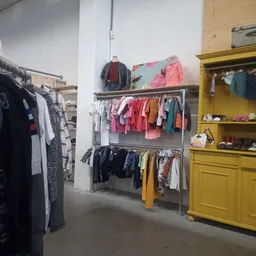 Rekken met tweedehands kinderkleding in verschillende kleuren, waaronder rode, roze, gele en blauwe items
