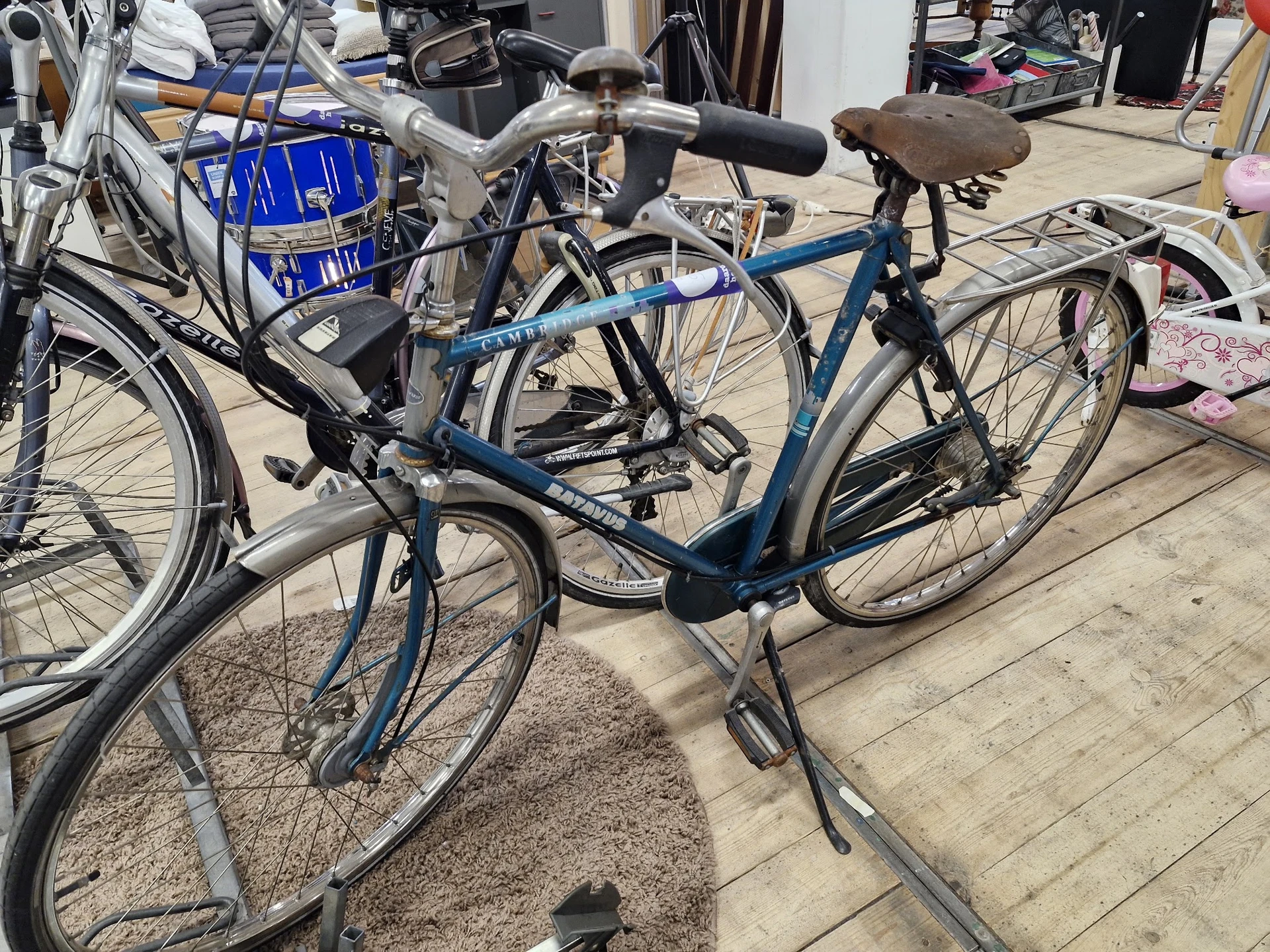 Tweedehands fietsen uitgestald op een terras, waaronder een blauwe damesfiets met bruin zadel op de voorgrond