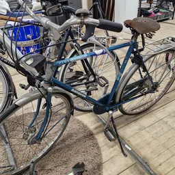 Tweedehands fietsen uitgestald op een terras, waaronder een blauwe damesfiets met bruin zadel op de voorgrond