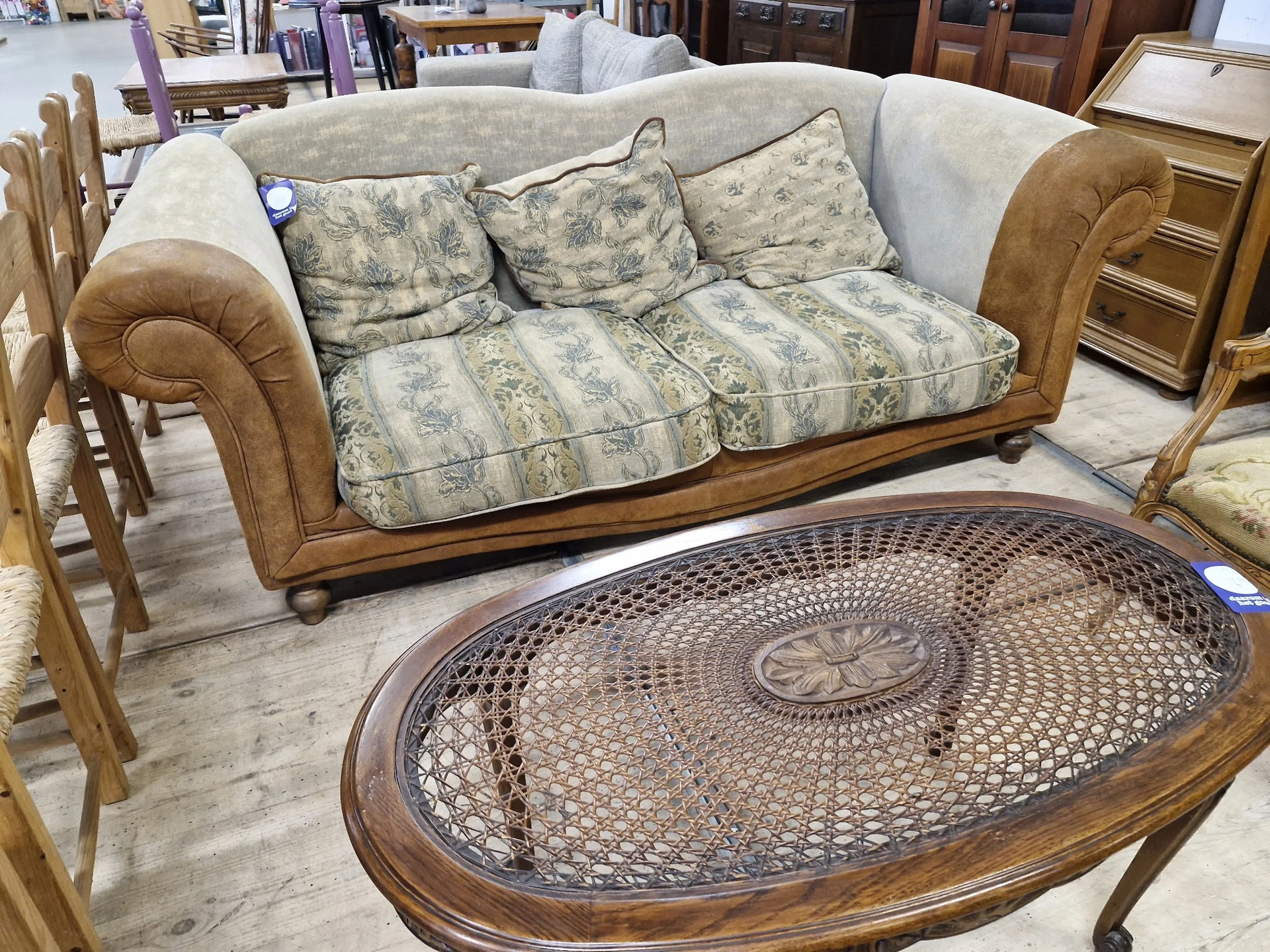 Houten meubels in kringloopwinkel: een sofa met kussens en een ovale salontafel met vlechtwerk