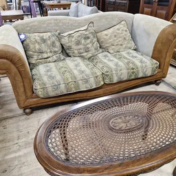 Houten meubels in kringloopwinkel: een sofa met kussens en een ovale salontafel met vlechtwerk