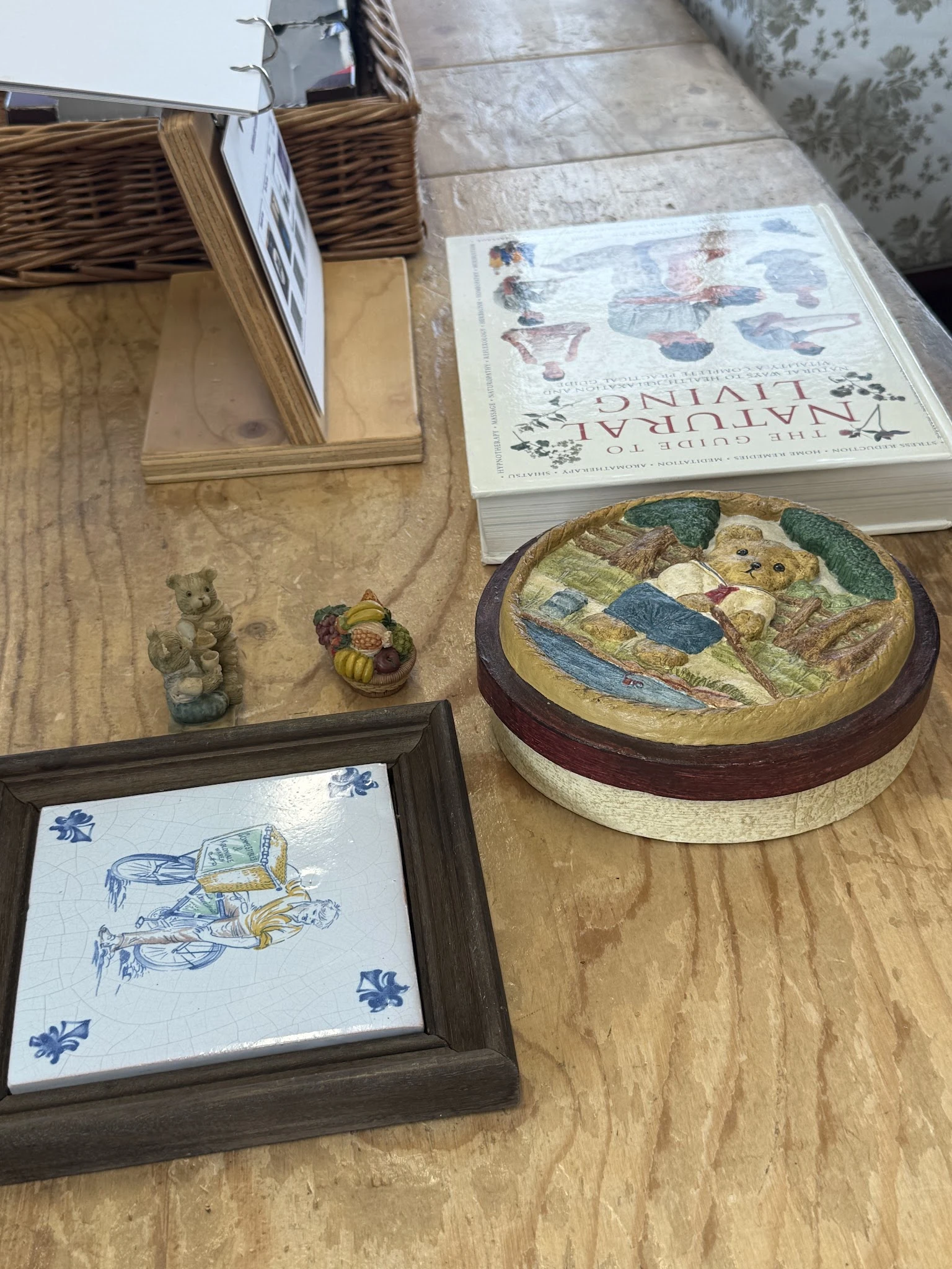 Uitgestalde tweedehands artikelen op houten tafel: kleine beeldjes, decoratief borduurwerk en een ronde decoratieve schaal me