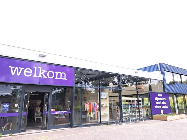 Gevel van kringloopwinkel met paarse welkom-opschrift en grote ramen met uitstallingen