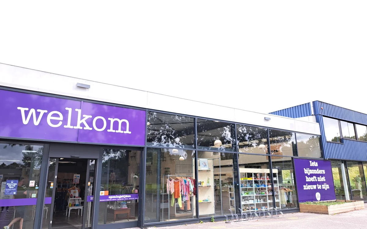 Gevel van kringloopwinkel met paarse welkom-opschrift en grote ramen met uitstallingen