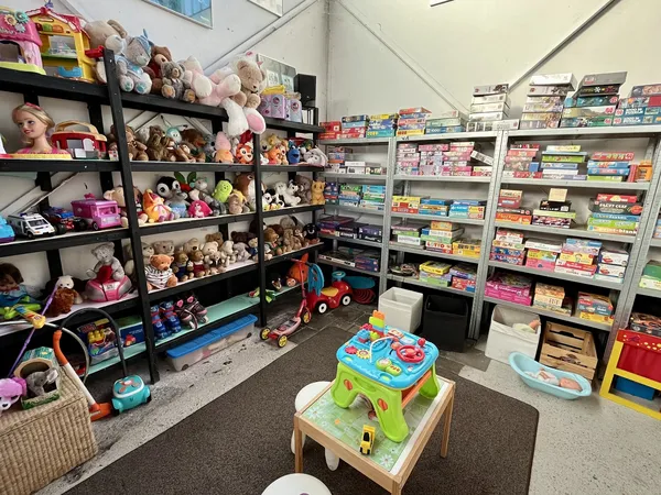 Speelgoedafdeling met zwarte stellingen vol knuffels en poppen, witte kastjes met boeken en spelletjes, en speelgoed op de vl