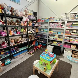 Speelgoedafdeling met zwarte stellingen vol knuffels en poppen, witte kastjes met boeken en spelletjes, en speelgoed op de vl