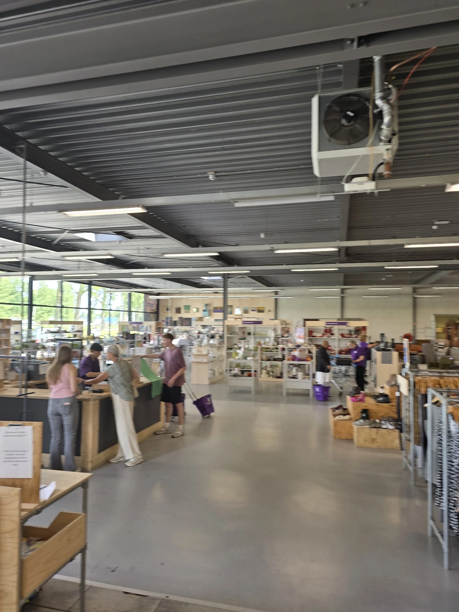 Ruim winkelinterieur met bezoekers bij toonbanken en diverse uitgestalde artikelen tegen de muren