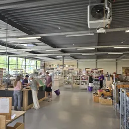 Ruim winkelinterieur met bezoekers bij toonbanken en diverse uitgestalde artikelen tegen de muren