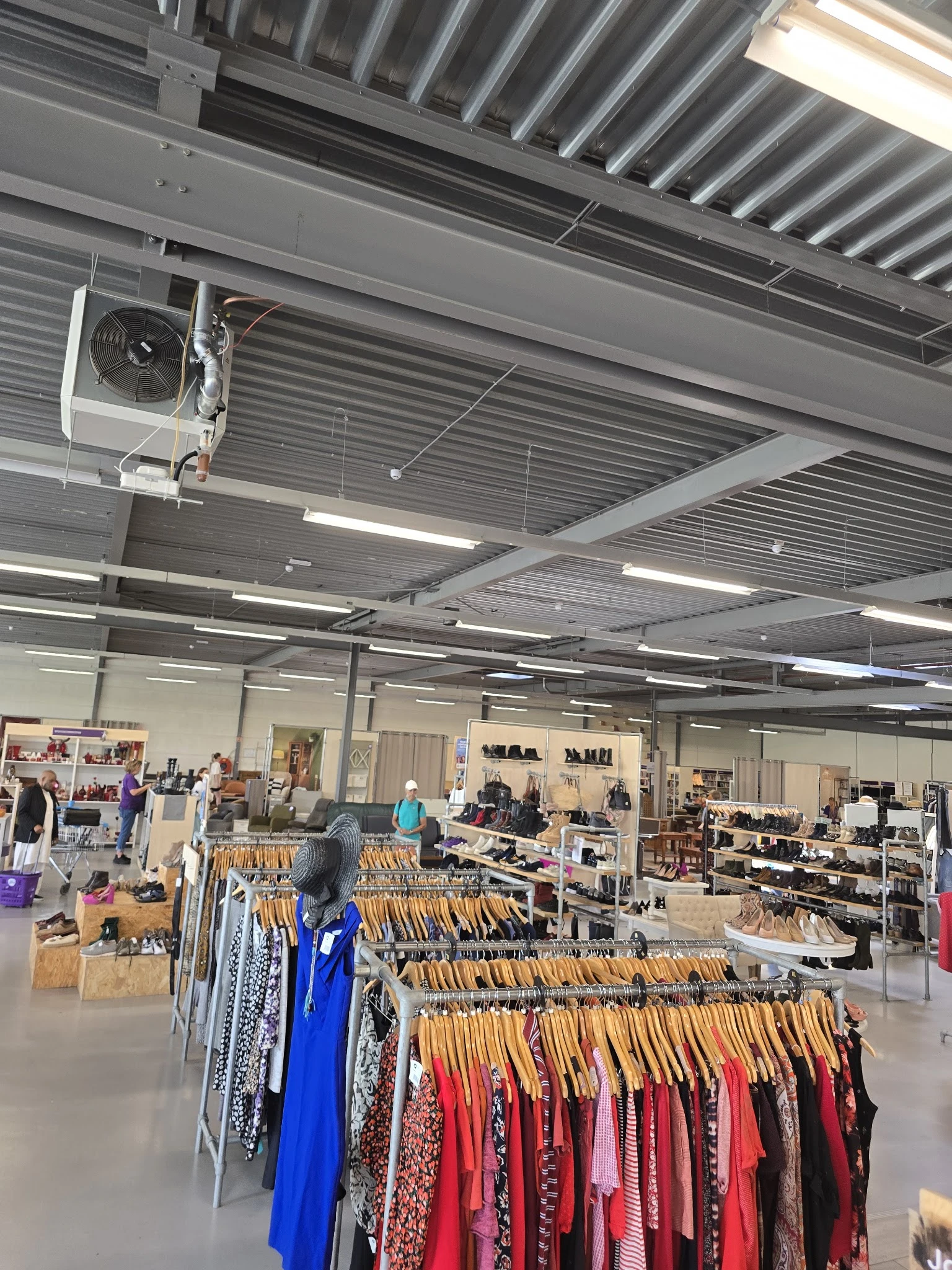 Winkelvloer van kringloopwinkel met kledingrekken, toonbanken en bezoekers onder stalen plafond