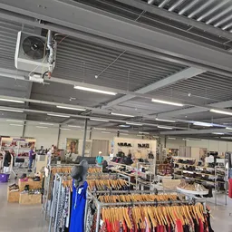 Winkelvloer van kringloopwinkel met kledingrekken, toonbanken en bezoekers onder stalen plafond