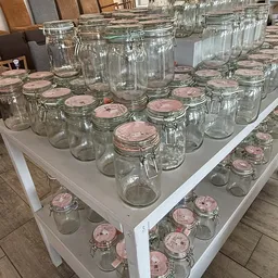 Glazen potten en jars met roze deksels uitgestald op witte tafels