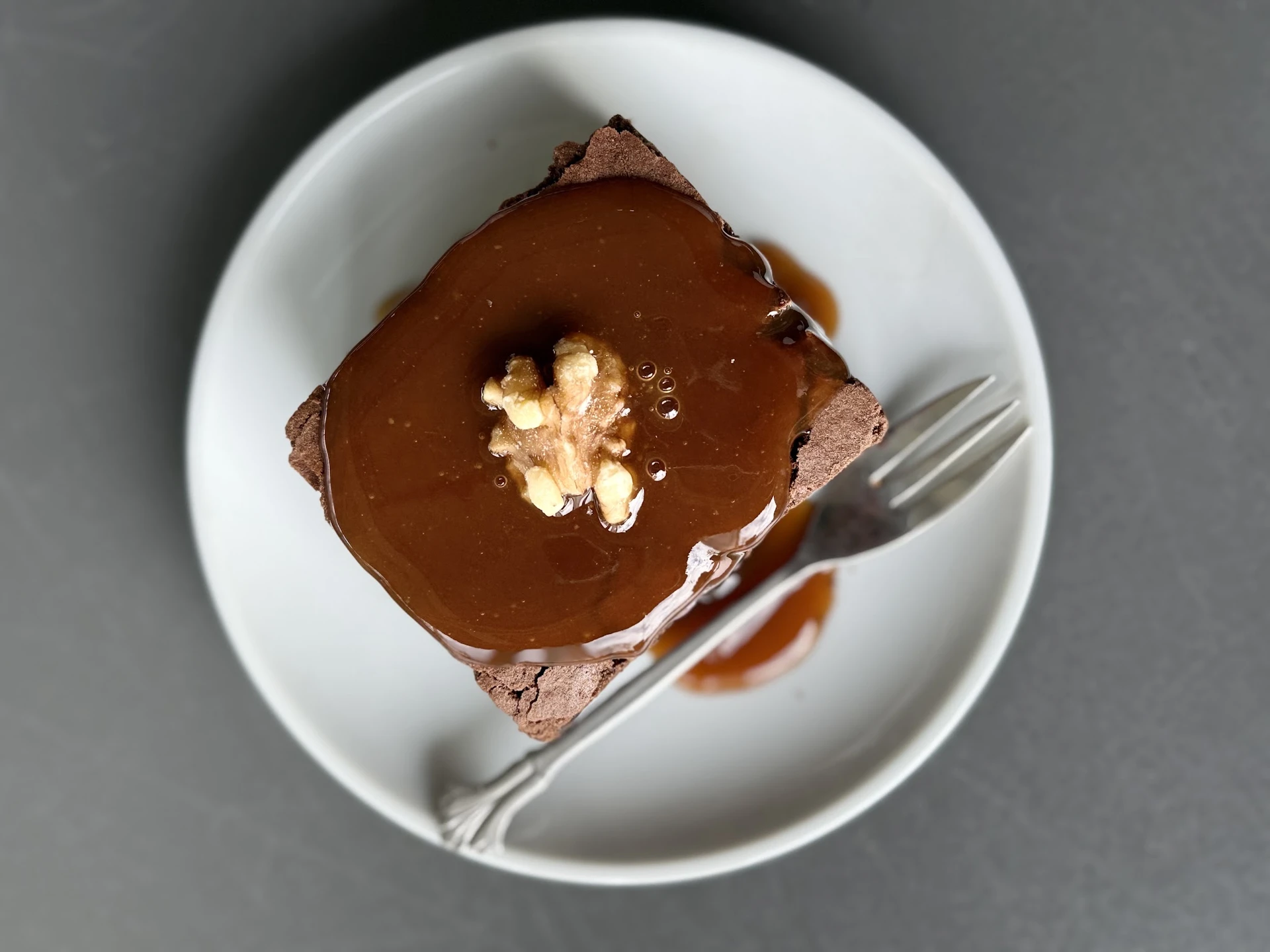 Chocoladetaart met karamel glazuur en walnoot garnering op wit bord met vork