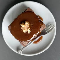 Chocoladetaart met karamel glazuur en walnoot garnering op wit bord met vork