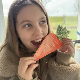 Meisje houdt papieren wortel omhoog en lacht naar camera