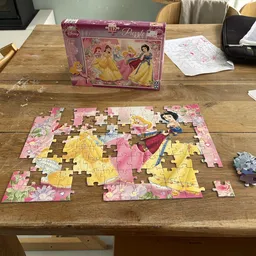 Partially completed Disney Princess puzzle on wooden table with box and loose pieces